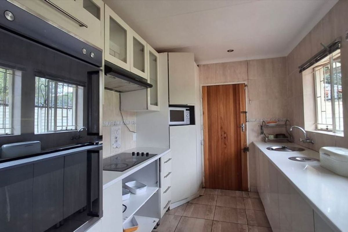 A functional kitchen featuring built-in cabinetry, an integrated oven, electric cooktop, and double sink with tiled finishes throughout.