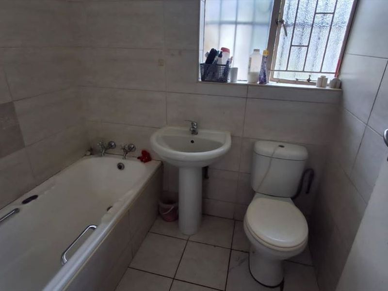 A functional bathroom featuring a pedestal basin, bathtub, and toilet with neutral wall and floor tiling.