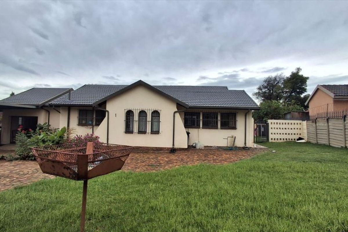Rear view of a single-story house featuring a tiled roof, paved outdoor area, and secure boundary walling.