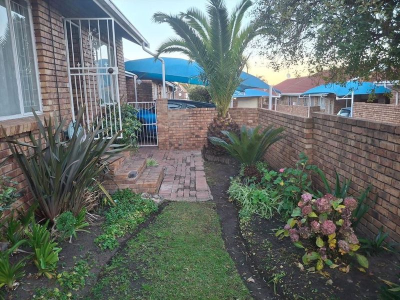 Front entrance area featuring a brick facade, security gate, and a small landscaped garden with brick paving.