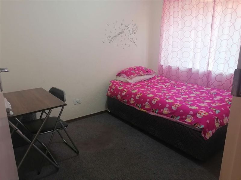 A standard bedroom featuring carpeted flooring and a window with curtains, providing a functional space for a single bed and study area.