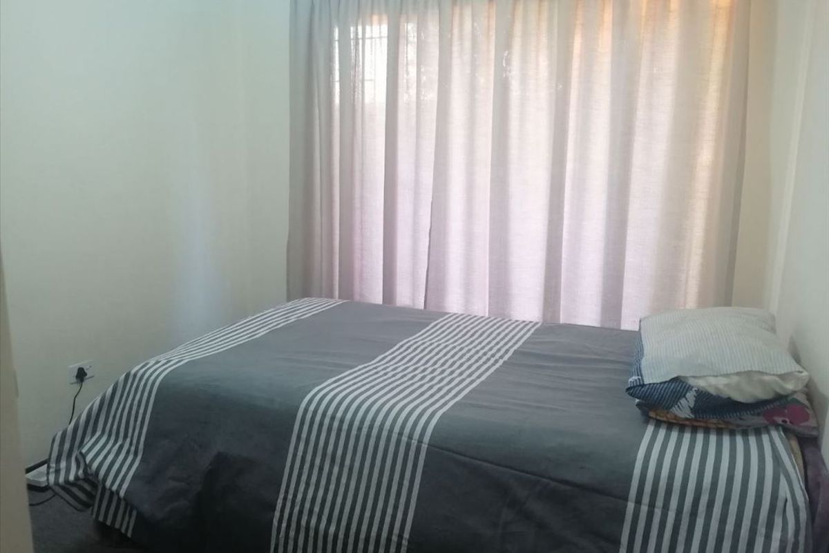 A standard bedroom featuring neutral walls, carpeted flooring, and a window dressed with floor-length curtains.
