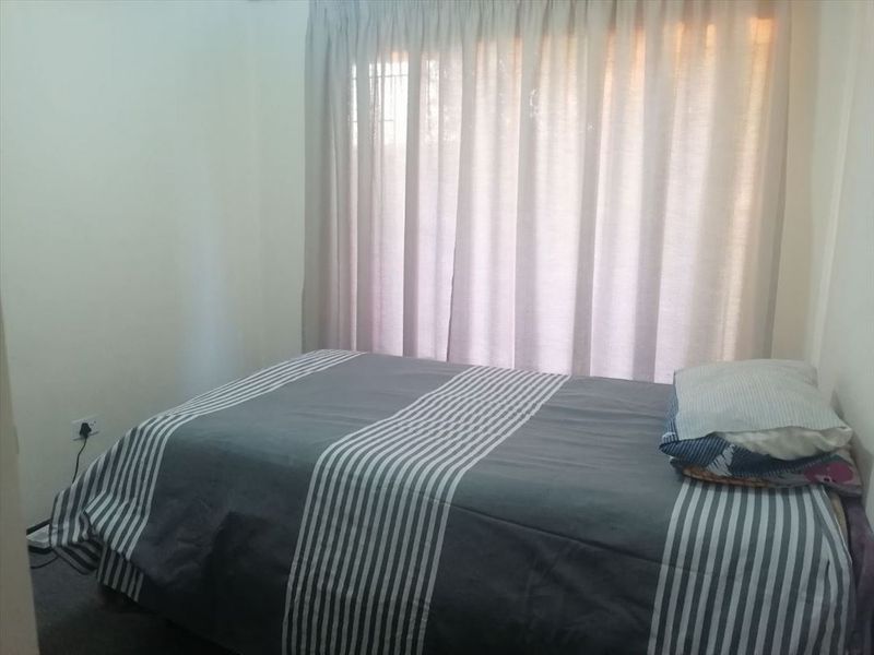 A standard bedroom featuring neutral walls, carpeted flooring, and a window dressed with floor-length curtains.