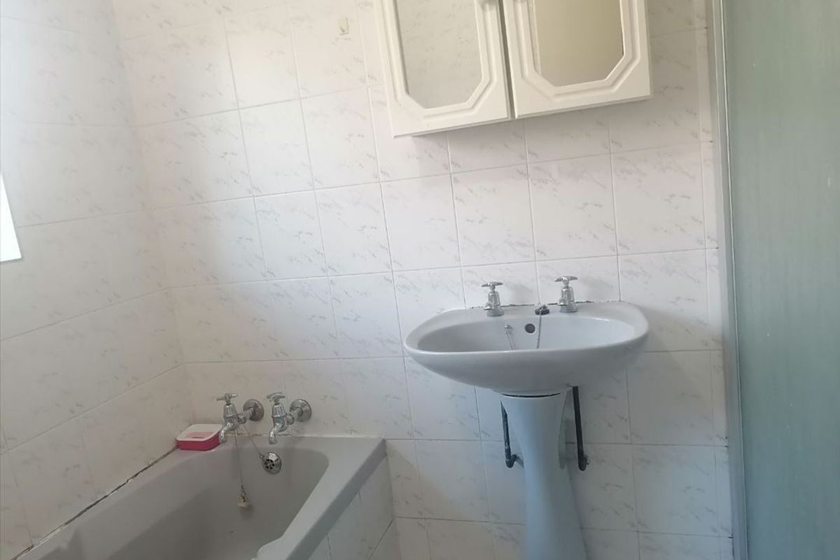 A dated bathroom featuring a pedestal basin, bathtub, and wall-mounted medicine cabinet with tiled walls and a shower enclosure.