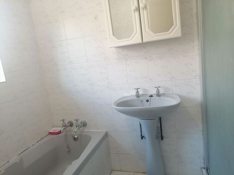 A dated bathroom featuring a pedestal basin, bathtub, and wall-mounted medicine cabinet with tiled walls and a shower enclosure.