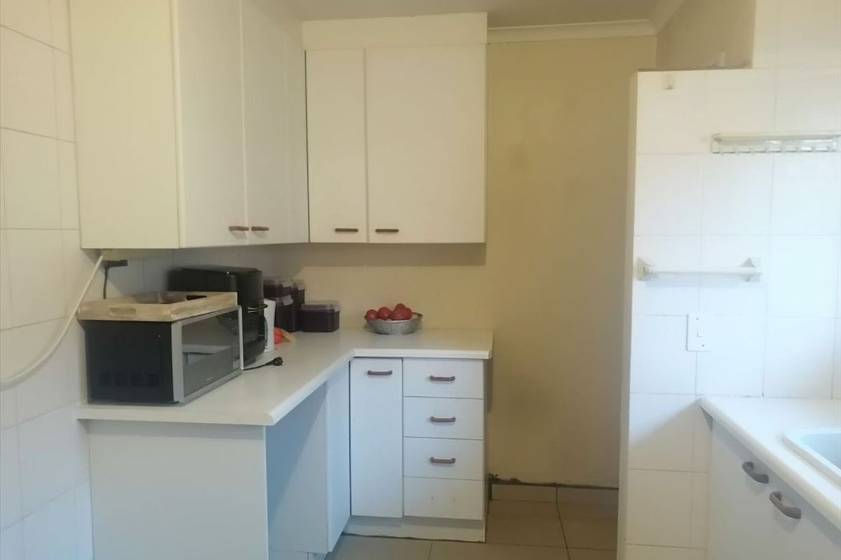 A functional kitchen featuring white built-in cabinetry, laminate countertops, and tiled splashbacks, offering a clean canvas for potential cosmetic updates.