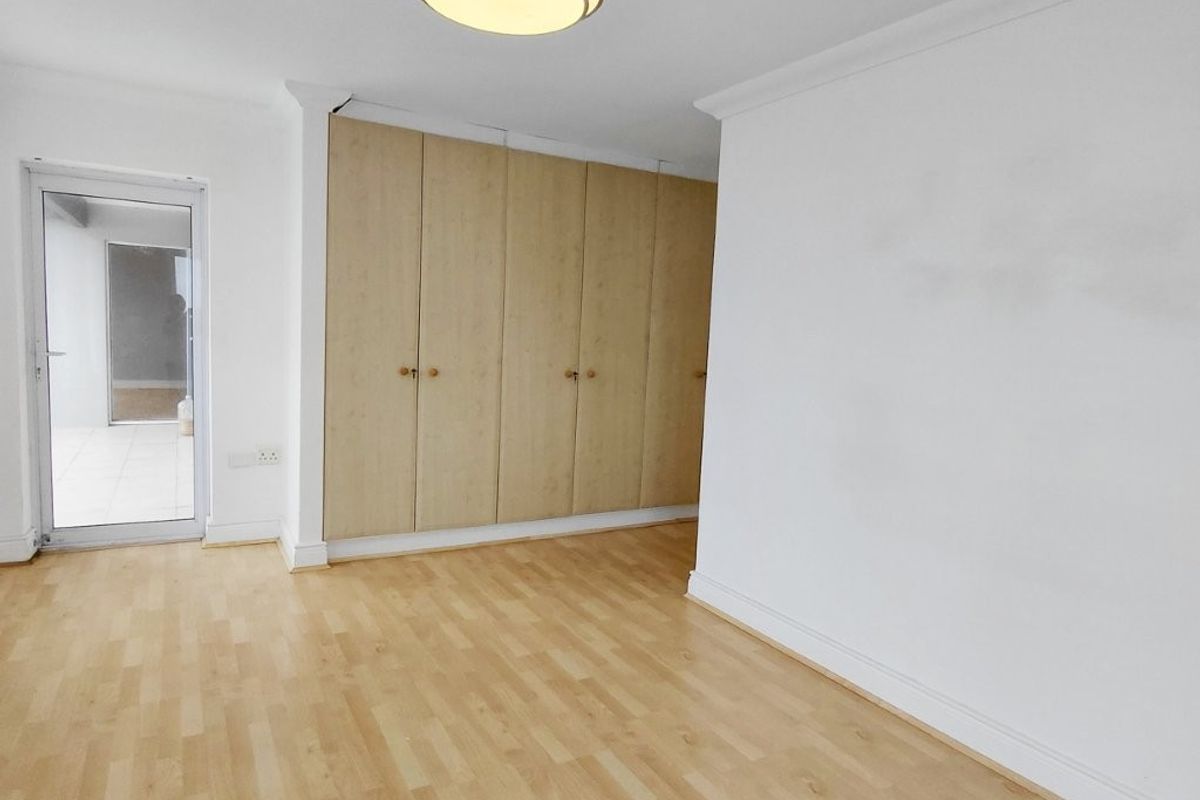 A bright, empty bedroom featuring light wood-look laminate flooring, built-in cupboards, and a glass door providing access to an outdoor area.