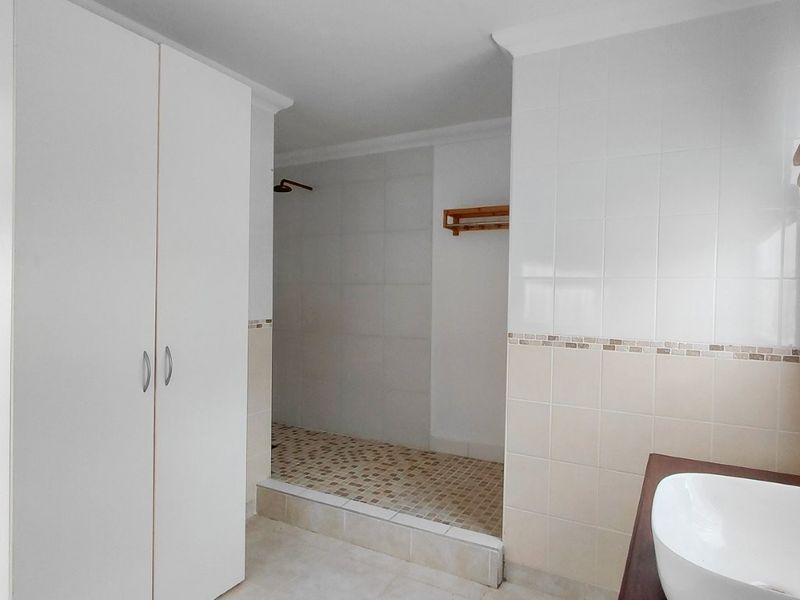 A clean, functional bathroom featuring a walk-in shower, vanity basin, and built-in storage cupboard with neutral wall and floor tiling.