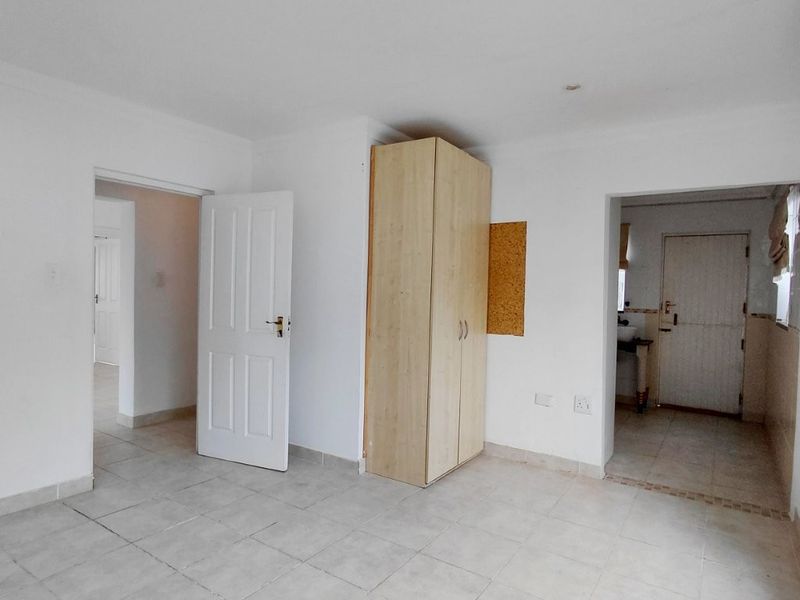 A bright, empty living area featuring neutral tiled flooring and a built-in cupboard, providing a clean and versatile space.