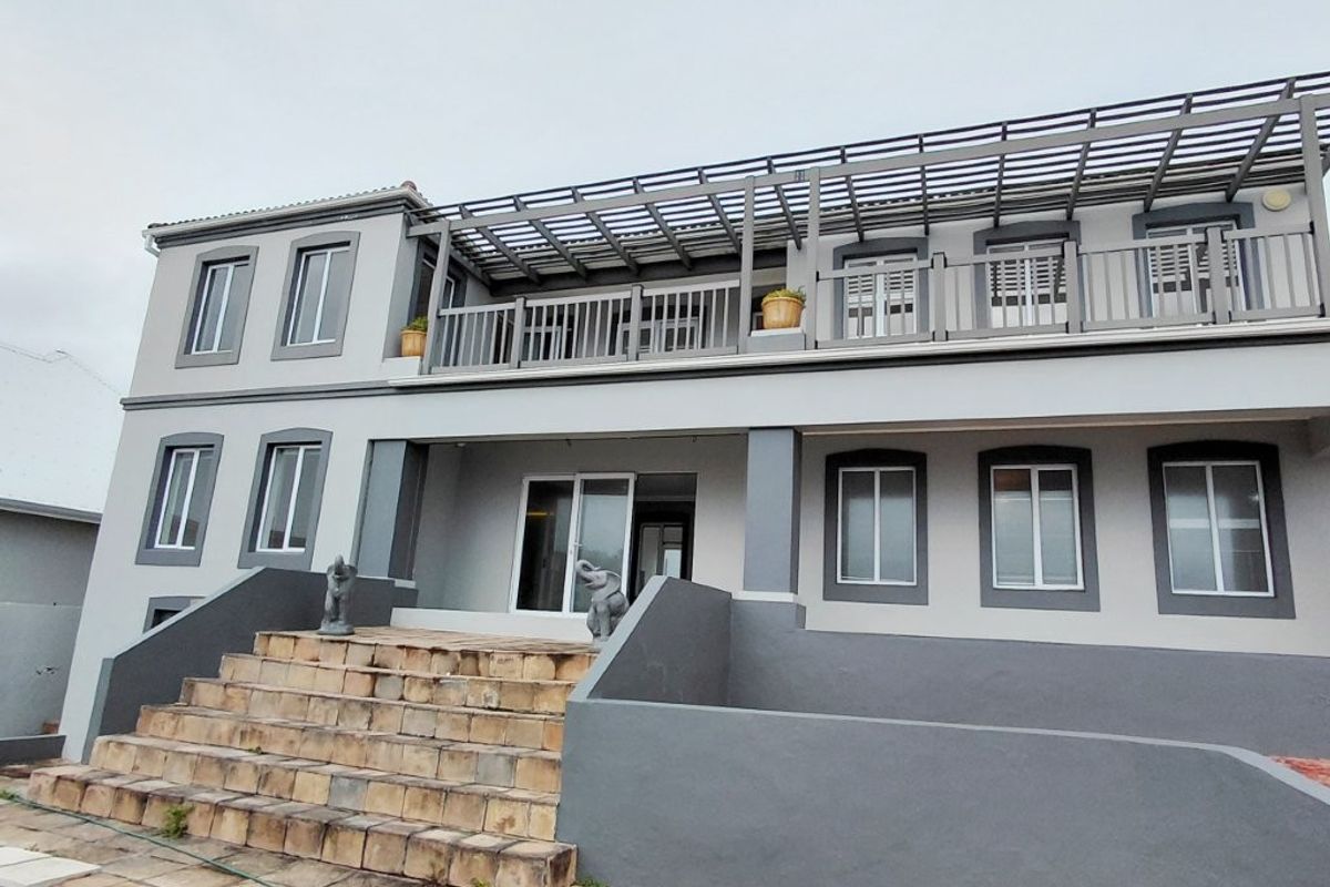 Rear elevation of a two-story house featuring a large stone staircase, a spacious upper balcony with a pergola, and paved patio area.