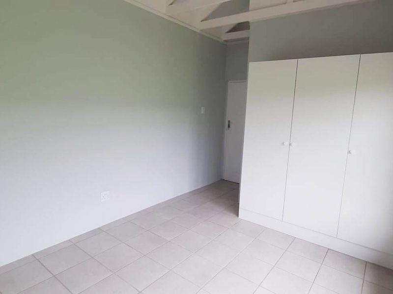 A bright, empty bedroom featuring neutral wall tones, tiled flooring, and a built-in white wardrobe with timber-framed windows.
