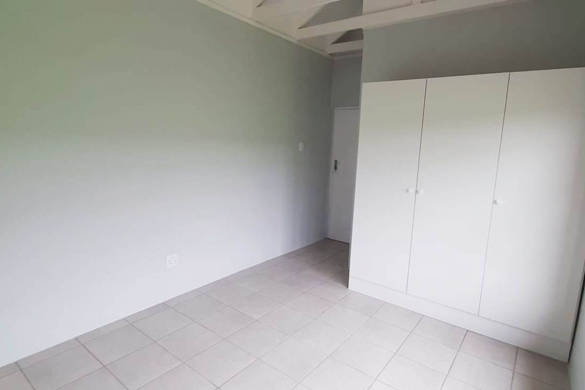A bright, empty bedroom featuring neutral wall tones, tiled flooring, and a built-in white wardrobe with timber-framed windows.