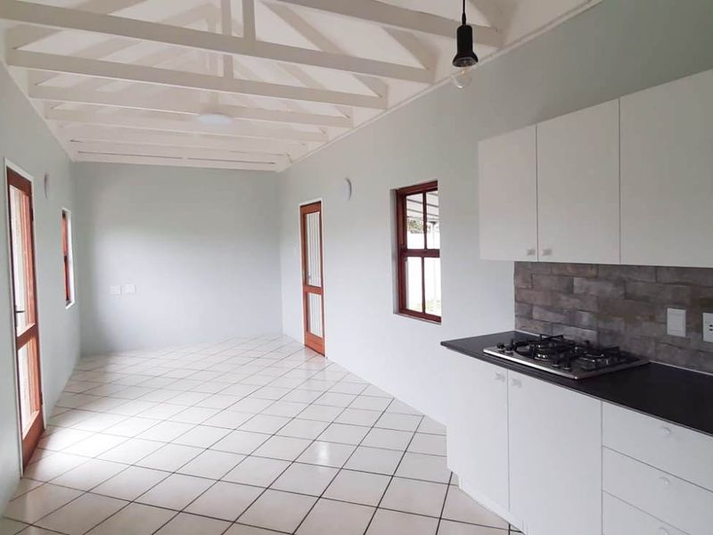 An open-plan living and kitchen area featuring exposed white timber beams, ceramic tiled flooring, and a modern kitchen with a gas hob.