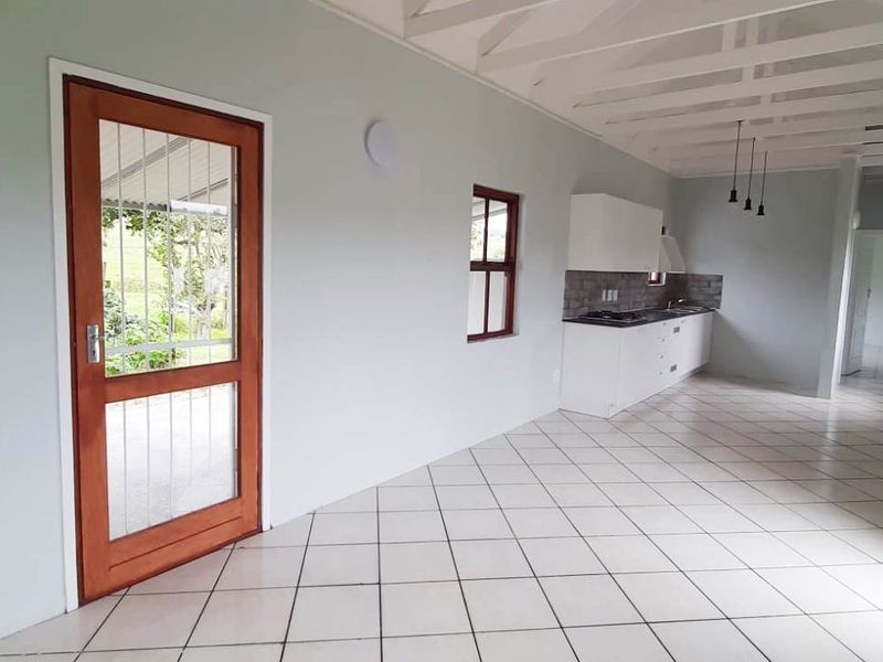 An open-plan living and kitchen area featuring tiled floors, exposed beam ceilings, and a functional kitchen layout with built-in cabinetry and appliances.