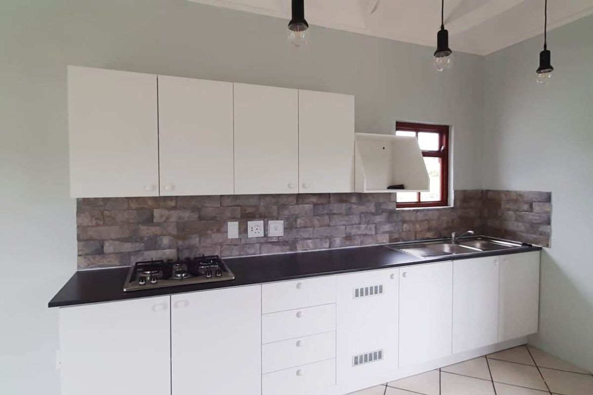 A clean, modern kitchen featuring white cabinetry, a gas hob, stone-look backsplash, and stainless steel sink, offering a bright and functional workspace.