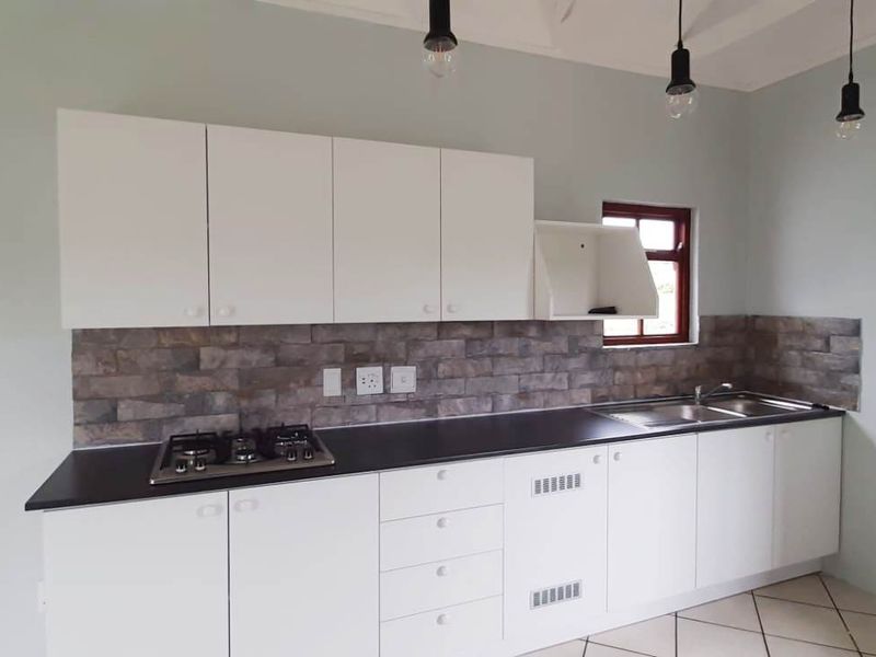 A clean, modern kitchen featuring white cabinetry, a gas hob, stone-look backsplash, and stainless steel sink, offering a bright and functional workspace.