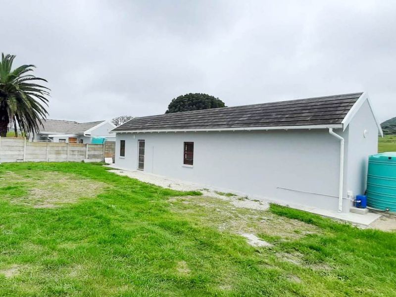Rear view of the property featuring a grey exterior finish, tiled roof, and a large water tank set within a spacious grassed yard.