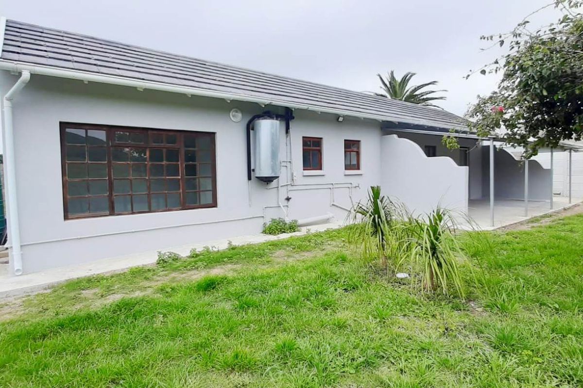 Rear view of the house featuring a tiled roof, exterior water tank, solar geyser, and a covered patio area overlooking the garden.
