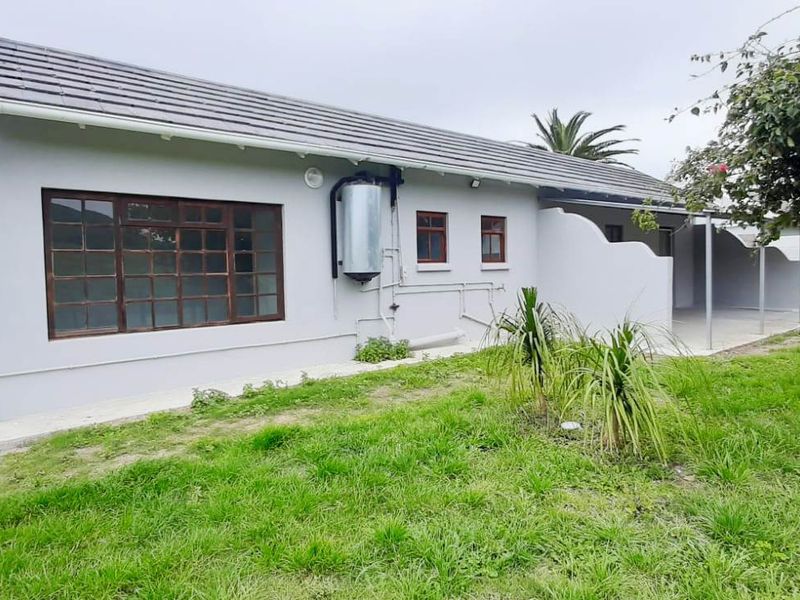 Rear view of the house featuring a tiled roof, exterior water tank, solar geyser, and a covered patio area overlooking the garden.