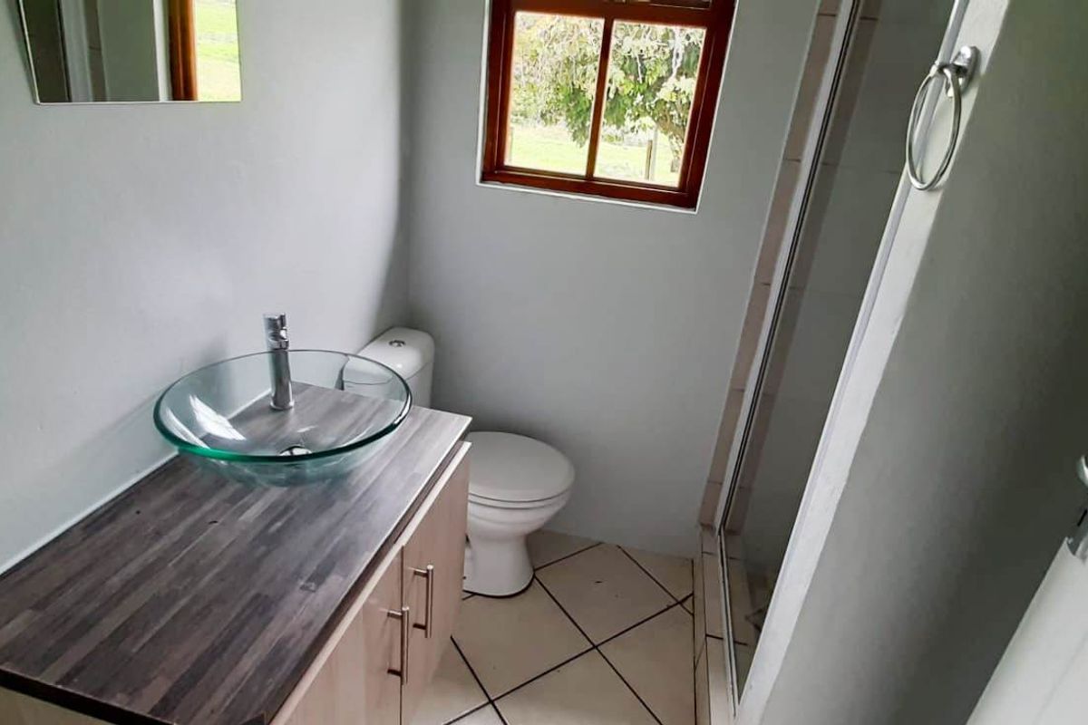 A functional bathroom featuring a glass vessel sink on a wood-look vanity, a toilet, and a glass-enclosed shower with tiled flooring.