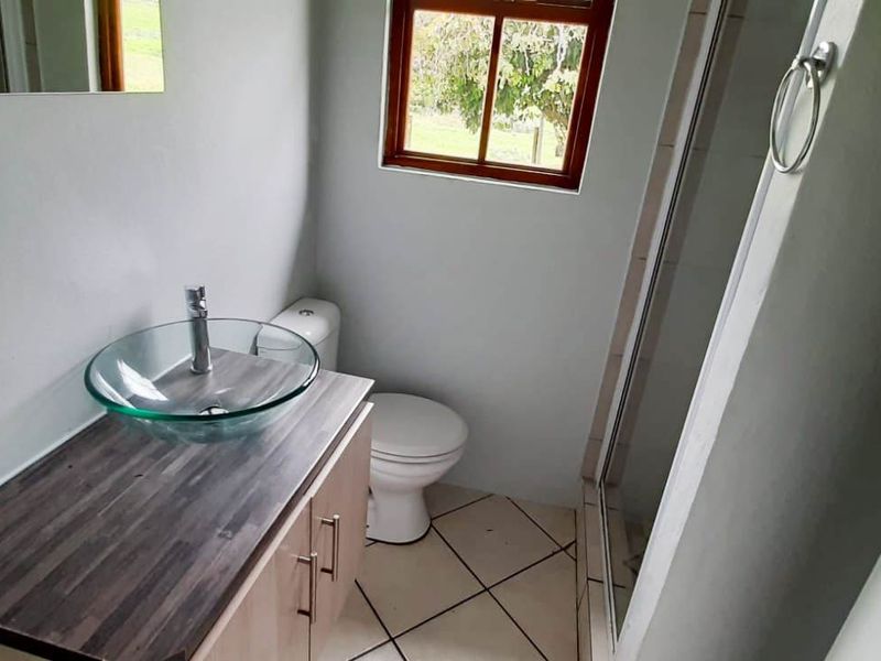 A functional bathroom featuring a glass vessel sink on a wood-look vanity, a toilet, and a glass-enclosed shower with tiled flooring.