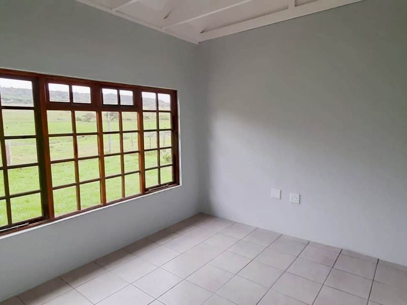 A bright, empty bedroom featuring ceramic floor tiles, an exposed beam ceiling, and a large timber-framed window with scenic rural views.