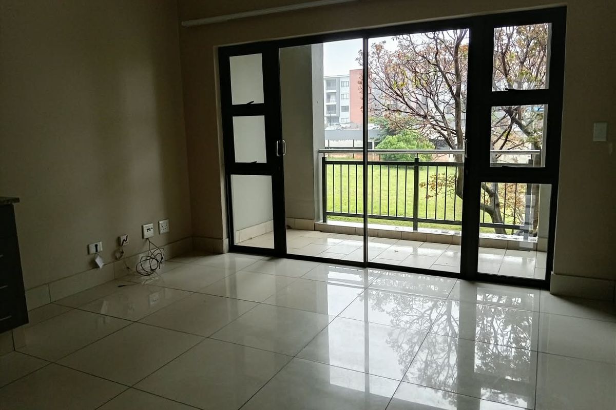 An empty living room featuring polished tile floors and a large sliding glass door that opens onto a private balcony with neighborhood views.