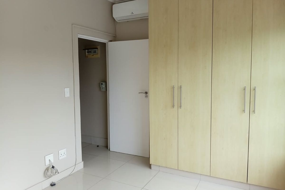 A clean, empty bedroom featuring light-toned built-in cupboards, tiled flooring, and a wall-mounted air conditioning unit.