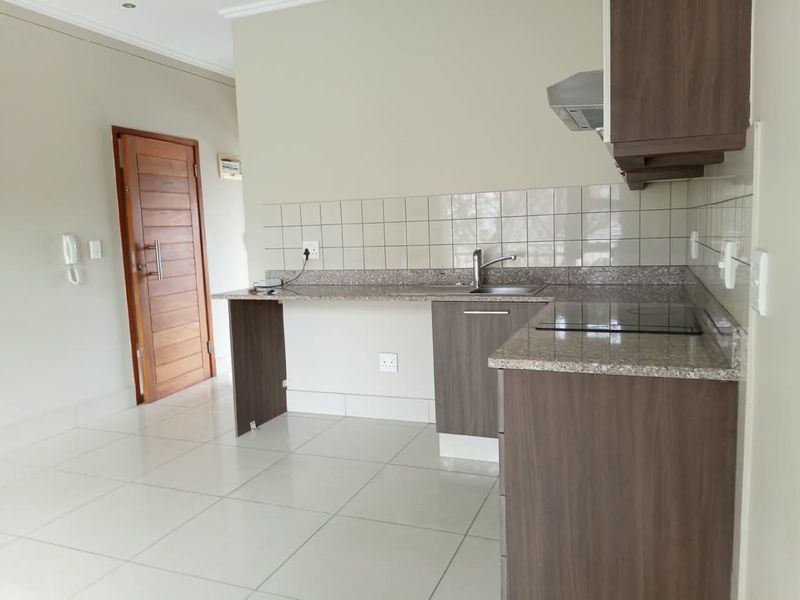 A clean, modern kitchen featuring granite countertops, built-in cabinetry, an electric hob, and tiled flooring in an open-plan layout.