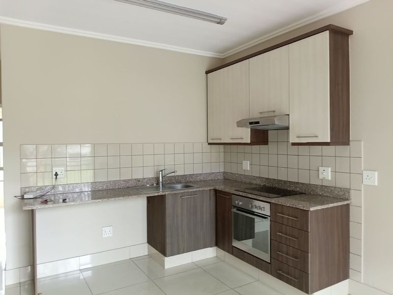 A clean, modern kitchen featuring two-tone cabinetry, granite countertops, a built-in oven, electric hob, and tiled backsplash.