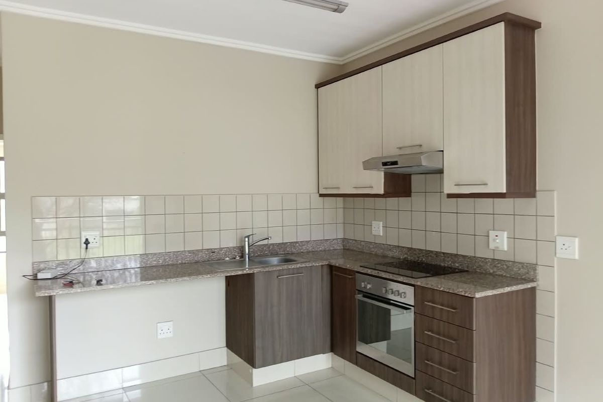A clean, modern kitchen featuring two-tone cabinetry, granite countertops, a built-in oven, electric hob, and tiled backsplash.