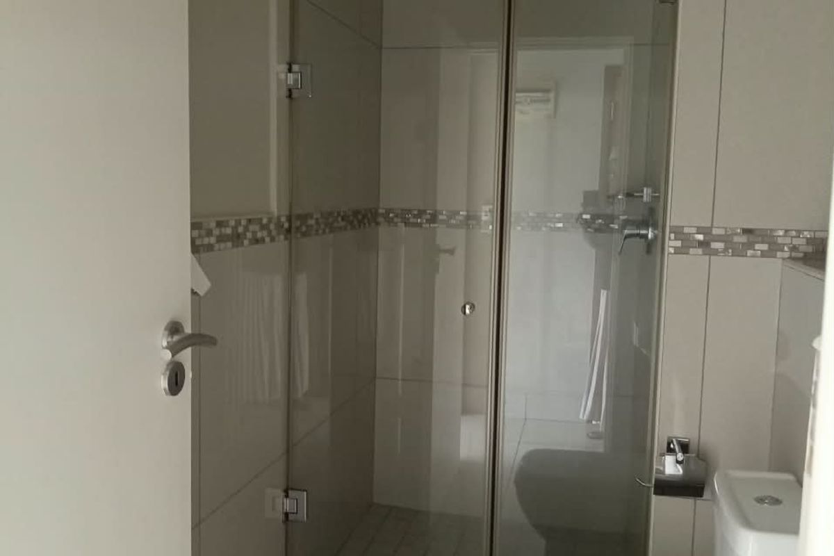 A clean, modern bathroom featuring a glass-enclosed shower, neutral wall tiles with a decorative mosaic border, and standard sanitary fixtures.