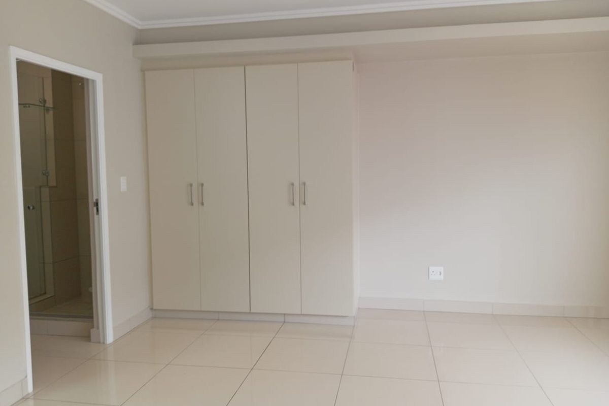 A clean, empty bedroom featuring neutral tiled flooring, built-in cupboards, and direct access to an en-suite bathroom.