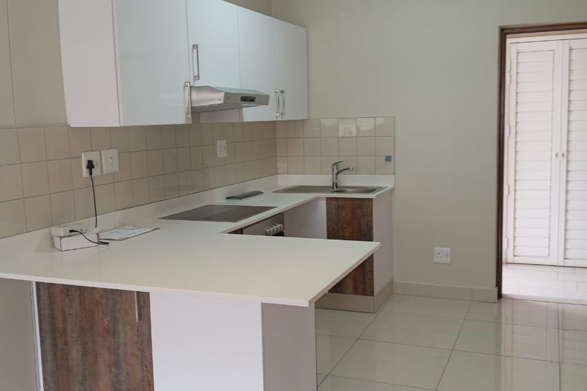 A clean, modern kitchen featuring white and wood-tone cabinetry, integrated appliances, tiled flooring, and a functional breakfast bar layout.