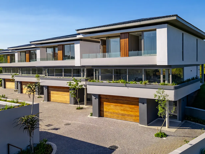 Modern multi-level residential complex featuring contemporary architecture, timber garage doors, glass-fronted balconies, and paved driveway access.