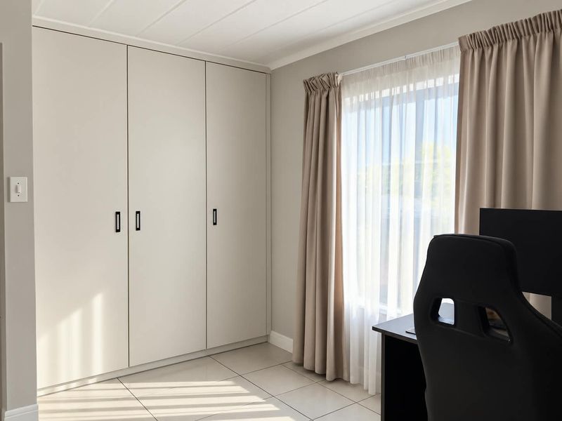 A bright bedroom featuring neutral walls, large built-in cupboards, and light-colored floor tiles, offering a clean and modern aesthetic.