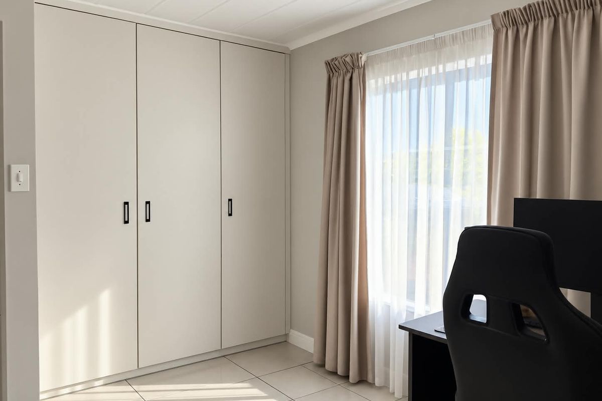 A bright bedroom featuring neutral walls, large built-in cupboards, and light-colored floor tiles, offering a clean and modern aesthetic.