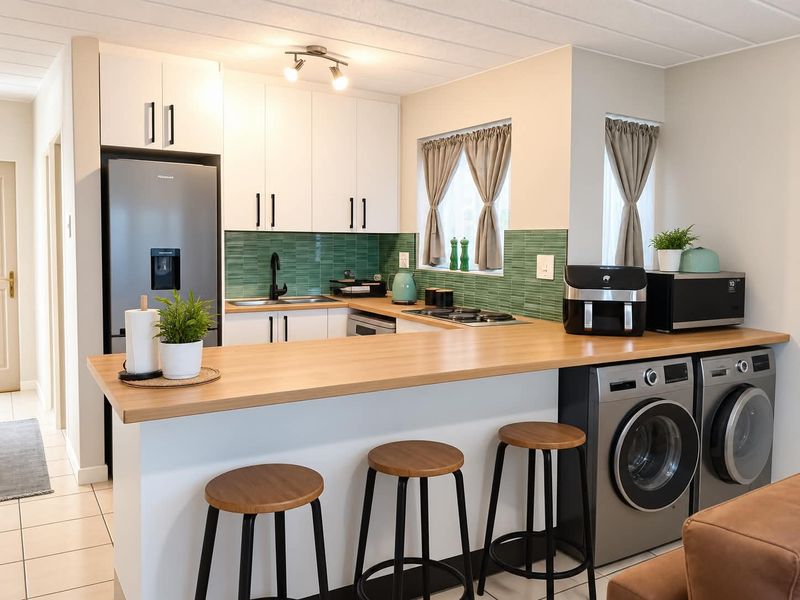 Modern kitchen featuring white cabinetry, a wooden breakfast bar, green tiled backsplash, and integrated laundry appliances.