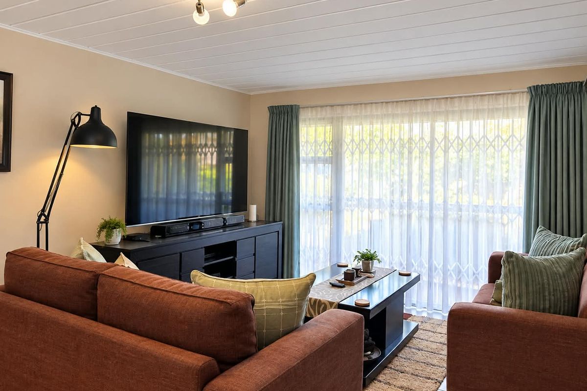 A comfortable living room featuring tiled flooring, a large sliding glass door with security gate, and neutral wall finishes.