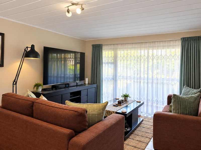 A comfortable living room featuring tiled flooring, a large sliding glass door with security gate, and neutral wall finishes.