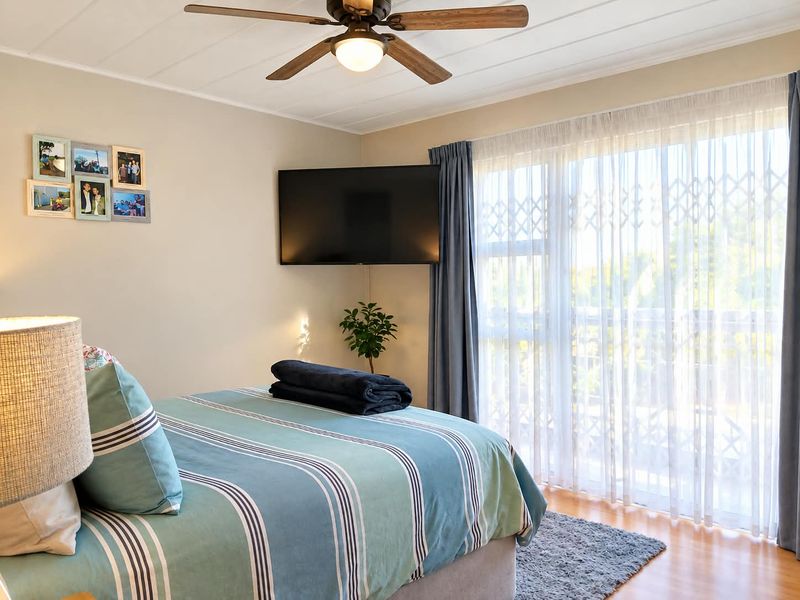 A well-maintained bedroom featuring a ceiling fan, laminate flooring, and a sliding glass door with a security gate leading to an outdoor area.