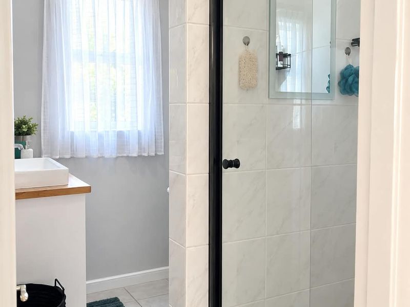 A modern bathroom featuring a walk-in shower with a black frame, a vanity with a vessel sink, and neutral tiled finishes.