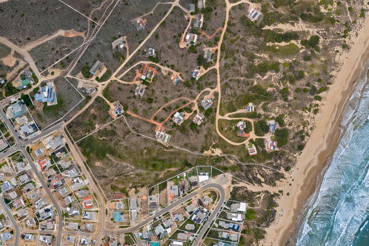Aerial view of a coastal residential area featuring vacant land plots, unpaved access roads, and proximity to the beach.