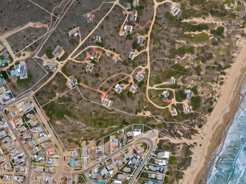 Aerial view of a coastal residential area featuring vacant land plots, unpaved access roads, and proximity to the beach.