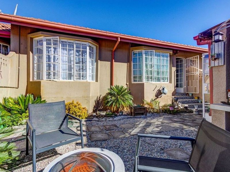 Rear exterior view of the apartment featuring bay windows, a paved courtyard area, and secure gated access.