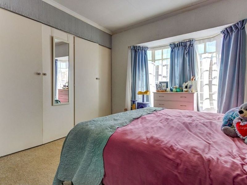 A bedroom featuring built-in cupboards and a bay window, providing natural light. The space includes carpeted flooring and requires minor cosmetic updates.