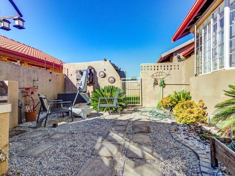 A private rear courtyard featuring a built-in braai, gravel landscaping, and paved pathways, enclosed by boundary walls with a secure metal gate.