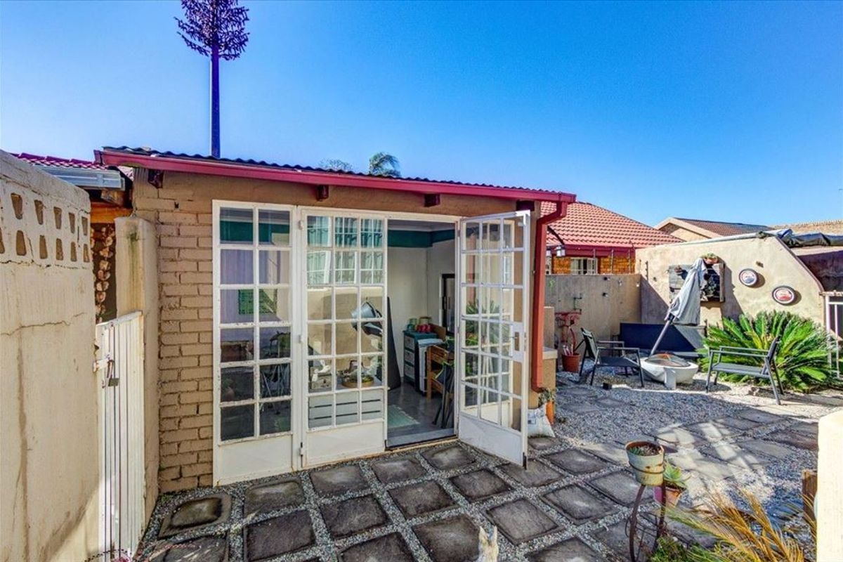 A rear exterior view featuring a paved patio area, gravel landscaping, and french doors leading into the property.