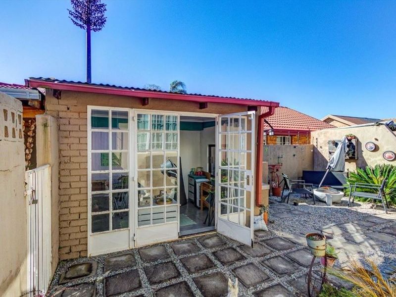 A rear exterior view featuring a paved patio area, gravel landscaping, and french doors leading into the property.