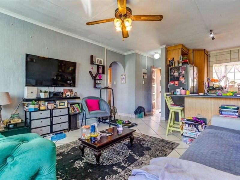 Open-plan living area featuring tiled flooring, a ceiling fan, and an integrated kitchen with a breakfast bar.